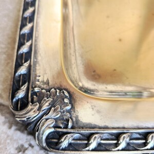 May include: Close-up of a silver serving tray with an ornate, detailed border. The tray has a rectangular shape and a smooth, polished surface.