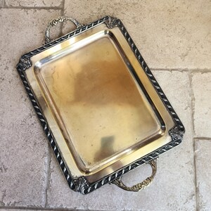 May include: A gold serving tray with a black rope design border and two ornate handles.