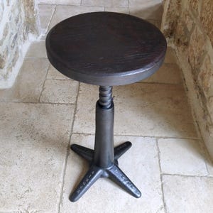 May include: A dark brown, round wooden stool with a metal base. The stool has a threaded, adjustable height mechanism and a star-shaped base. The wooden seat is approximately 12 inches in diameter.