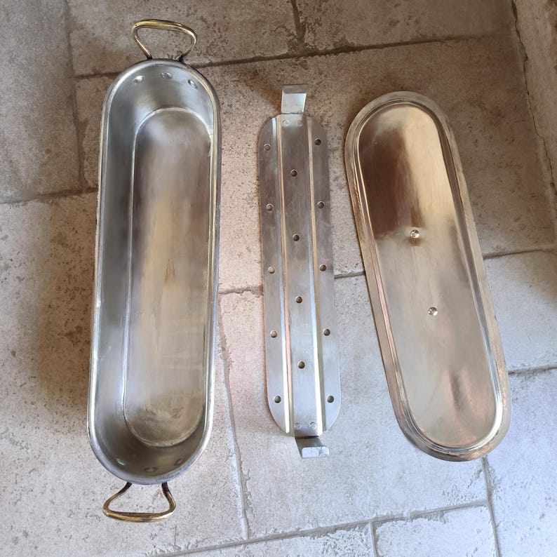 Puede incluir: Un conjunto de tres utensilios de cocina de metal vintage. El conjunto incluye una bandeja de horno larga y ovalada con asas de lat&oacute;n, un inserto de metal perforado y una tapa a juego. Los art&iacute;culos son de metal brillante de color plateado.