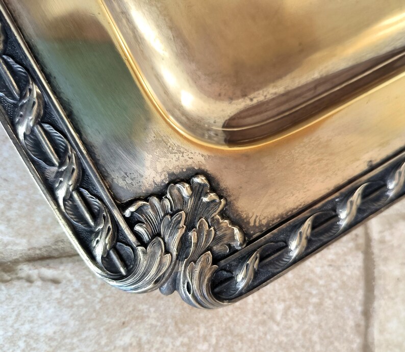 May include: A silver serving tray with a decorative border of stylized leaves and a gold-toned interior.