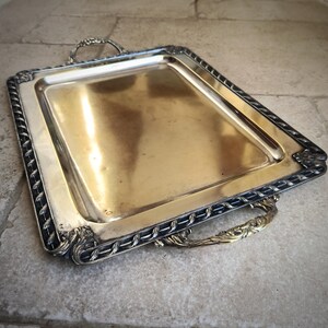 May include: A silver serving tray with a black rope design around the edge and two ornate brass handles.