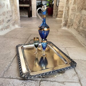 May include: A silver serving tray with a decorative border and two handles. The tray holds a blue glass decanter with gold accents and two matching blue and gold shot glasses.