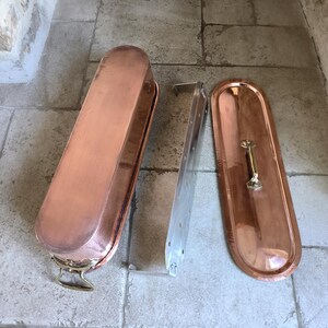 Puede incluir: Una olla rectangular de color cobre con tapa y rejilla met&aacute;lica. La olla tiene extremos redondeados y un asa de lat&oacute;n en la tapa. La rejilla es de metal color plata.