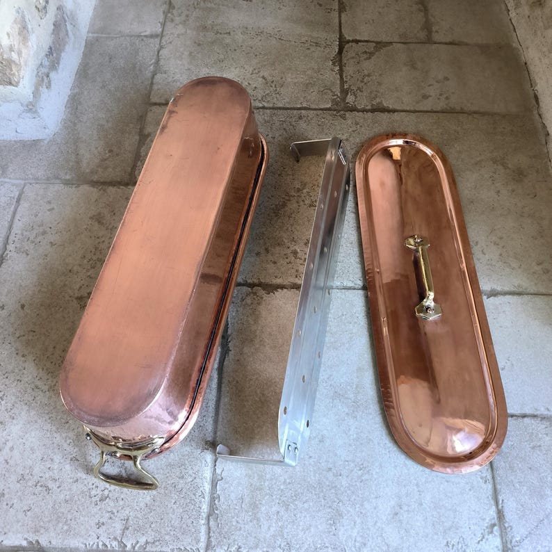 Puede incluir: Una olla rectangular de color cobre con tapa y rejilla met&aacute;lica. La olla tiene extremos redondeados y un asa de lat&oacute;n en la tapa. La rejilla es de metal color plata.