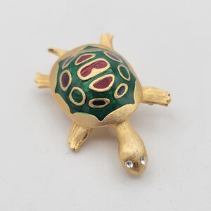 May include: A gold-toned turtle brooch with a green and red enamel shell and clear rhinestone eyes.