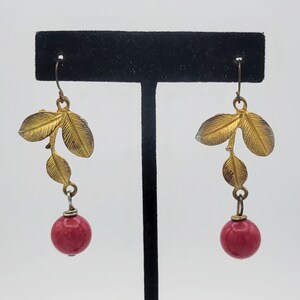 May include: Gold leaf earrings with a red bead dangle. The leaves are arranged in a branch-like pattern.
