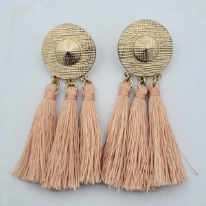 May include: A pair of gold tone earrings with three peach colored tassels hanging from each earring.