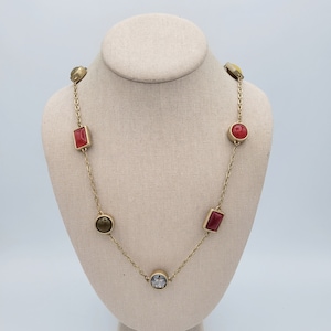 May include: A gold chain necklace with various colored stones. The stones are round and rectangular in shape. The necklace is on a mannequin.