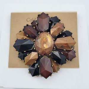 Peut inclure: Une grande broche de couleur marron et noire avec un motif floral. La broche est faite de pierres facettées en verre ou en plastique et a un sertissage en métal doré.