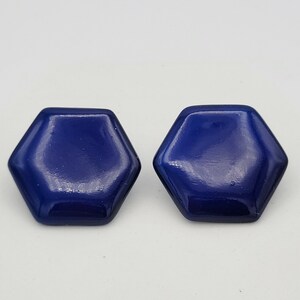 Op de afbeelding: Een paar donkerblauwe zeshoekige oorbel studs. De oorbellen zijn gemaakt van een glad, glanzend materiaal.