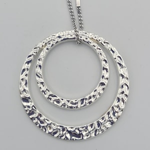 May include: A silver necklace featuring a textured double circle pendant. The circles are interlocked and have a hammered finish.