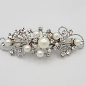 May include: Silver-toned hair barrette with a floral design. The barrette features faux pearls and clear and pink rhinestones. The barrette is approximately 4 inches long.