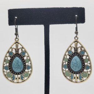 May include: A pair of dangle earrings with a turquoise blue stone set in a gold filigree design. The earrings have a green and blue enamel finish.