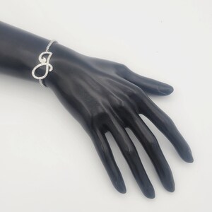 May include: A silver bracelet featuring a single letter 'J' charm, set with clear cubic zirconia stones. The bracelet is displayed on a black mannequin hand.