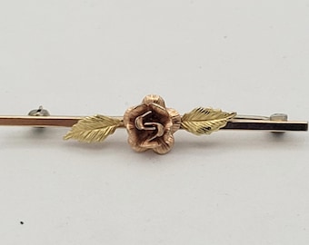 Peut inclure: Une broche en or et or rose avec une seule rose et des feuilles. La rose est au centre d'une fine barre.