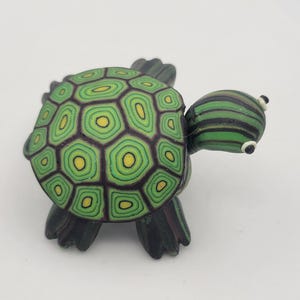 May include: A small green and black turtle figurine with a detailed shell pattern. The turtle has a striped head and black eyes.