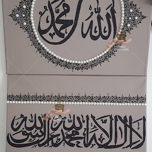May include: Two taupe canvas panels featuring black Arabic calligraphy. The top panel displays a circular design with a black lace border and white pearls. The bottom panel features a horizontal band of black calligraphy framed by white pearls.