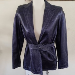 May include: A dark blue leather blazer with a belted waist. The blazer has a notched collar and long sleeves.