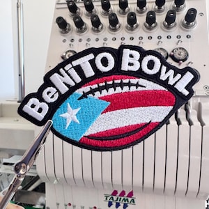 以下が含まれることがあります： 白い文字で「BeNiTo Bowl」と書かれた、フットボールの形をした刺繍パッチ。フットボールのデザインには、青い三角形、白い星、赤と白のストライプが特徴のプエルトリコの国旗が組み込まれています。