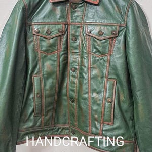 May include: A green leather jacket with brown stitching and metal buttons. The jacket has a denim-style design with two chest pockets and two front pockets. The text "HANDCRAFTING CORNER" is visible at the bottom of the jacket.