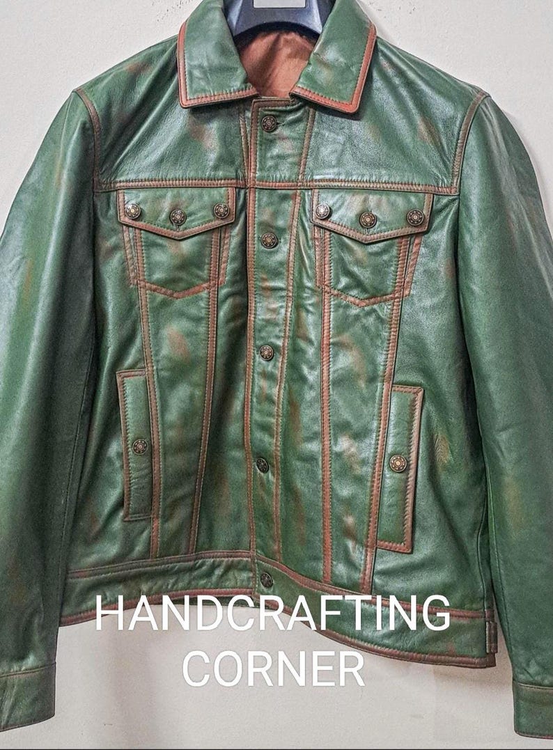 May include: A green leather jacket with brown stitching and metal buttons. The jacket has a denim-style design with two chest pockets and two front pockets. The text "HANDCRAFTING CORNER" is visible at the bottom of the jacket.