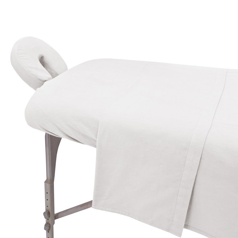 May include: White massage table with a white fitted sheet and a white face cradle.