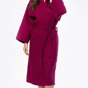 May include: A long, burgundy waffle weave robe with a self-tie belt and a patch pocket on the left side.