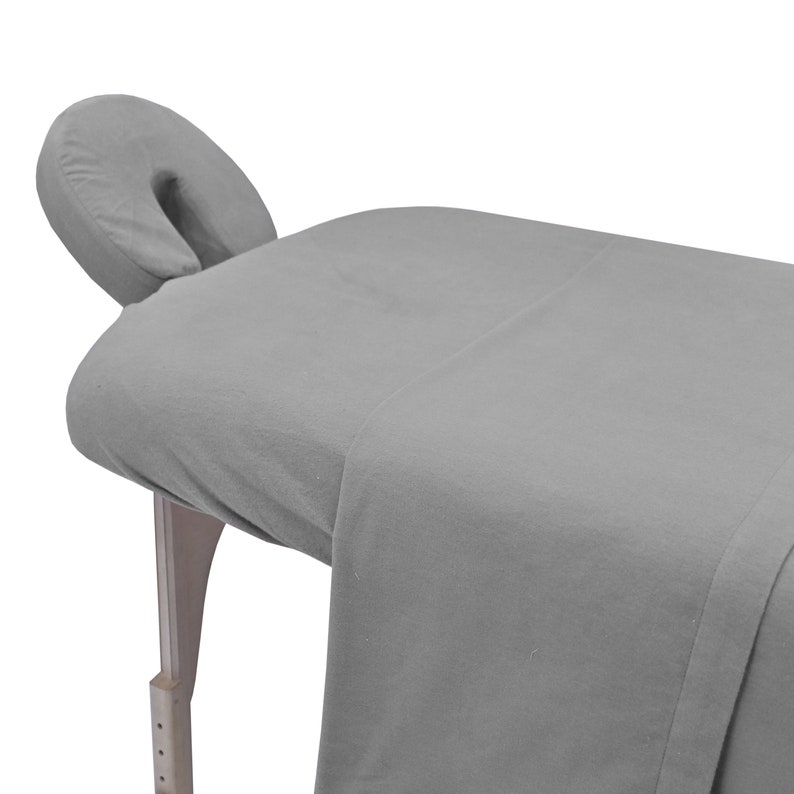 May include: Gray massage table with a gray fitted sheet and a gray face cradle.