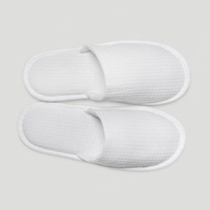 May include: A pair of white waffle-textured slippers. The slippers are open-toed and have a simple design.