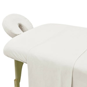 May include: White cotton massage table sheet with a white face cradle. The sheet is flat and smooth, and the face cradle is round and has a hole in the center.