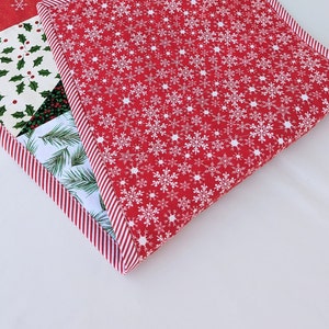 May include: A Christmas-themed quilted placemat with a red snowflake pattern and a striped border. Other sections feature holly, pine needles, and a red and white candy cane design. The placemat is square.