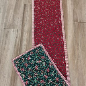 May include: Two Christmas-themed quilted table runners. One is rectangular with a red background and a pattern of small white and green floral designs. The other is square with a dark green background and a pattern of candy canes, holly, and stars. Both have a red and white striped border.