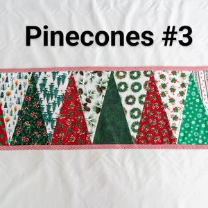 May include: A Christmas-themed table runner with a variety of festive patterns. The runner features alternating triangular sections with designs like Christmas trees, wreaths, and candy canes. The border is red and white striped, and the text "Pinecones #3" is at the top.