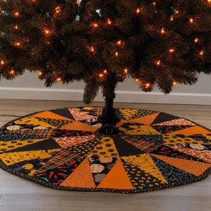May include: A circular fabric tree skirt featuring a patchwork design of various Halloween-themed patterns in orange, black, and yellow. The fabric segments include prints of pumpkins, candy corn, plaid, and chili peppers, finished with a dark border.