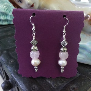 May include: A pair of silver dangle earrings with pink and white beads. The earrings feature a silver charm with a Celtic knot design.