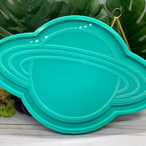 以下が含まれることがあります： リングが付いた惑星の形をしたターコイズブルーのシリコンモールド。このモールドは、レジンキャストと装飾品の作成のために設計されています。