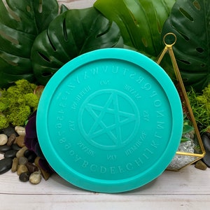May include: A turquoise blue silicone mold with a five-pointed star in the center and the letters of the alphabet surrounding the star. The mold is for making a resin or polymer clay pendant.