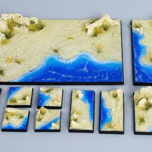 Puede incluir: Un conjunto de 10 baldosas de terreno con temática de arena y océano para juegos de mesa. Las baldosas están hechas de un material marrón claro con un diseño de ola oceánica azul. Las baldosas están dispuestas en un patrón de cuadrícula, con la baldosa más grande en el centro.