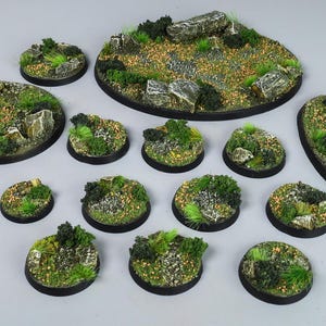 Puede incluir: Un conjunto de bases de terreno en miniatura, con varios tamaños y formas. Cada base está detallada con texturas realistas, incluyendo hierba verde, pequeñas rocas y parches de tierra. Las bases tienen un borde negro.