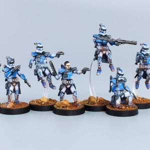 May include: A set of seven blue and white painted miniature figures of clone troopers from the Star Wars universe. The figures are posed in various action stances and are holding weapons. The figures are standing on round bases.