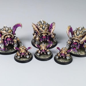 Puede incluir: Colección de seis criaturas de fantasía en miniatura, cada una con un caparazón espinoso detallado en tonos beige y morado. Las criaturas tienen amenazantes ojos rojos y están montadas sobre bases circulares.