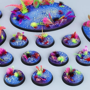 May include: A set of 15 blue and purple oval-shaped miniature gaming bases with black edges. The bases are decorated with colorful, textured, and glittery paint. The bases are covered in various shades of pink, blue, and green artificial foliage.
