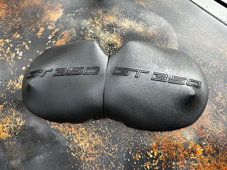 May include: Close-up of two black, rounded, textured motorcycle seat covers with the text "GT 350" embossed on each.