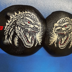 May include: Two black round patches featuring a white Godzilla-like monster graphic. The monster has red eyes and a red mouth. The patches have the number "7.3" in red on the side.