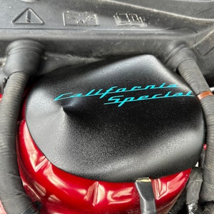 May include: Close-up of a black engine cover with the words "California Special" written in blue lettering.