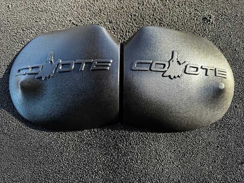 May include: Two black plastic engine covers with the word "Coyote" embossed on each. The word is in a stylized font with a coyote silhouette in the middle of the word.