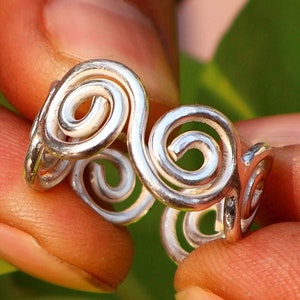Op de afbeelding: Een zilveren ring met een draaiend ontwerp. De ring is gemaakt van meerdere in elkaar verweven spiralen.