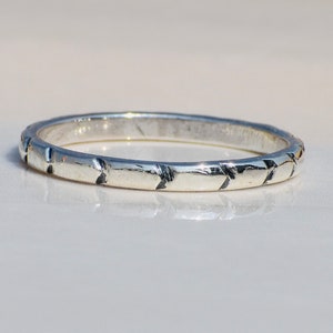 Könnte beinhalten: Ein silberner Bandring mit einem strukturierten Design. Der Ring ist schlicht und elegant.