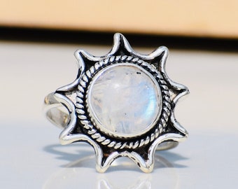 May include: A silver ring featuring a white moonstone set in a sunburst design.